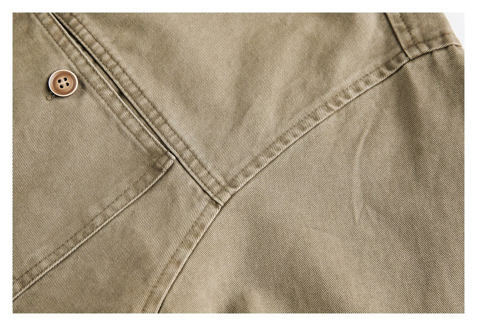 Close-up of tan shirt fabric and intersecting stitched seams, with one brown button visible.