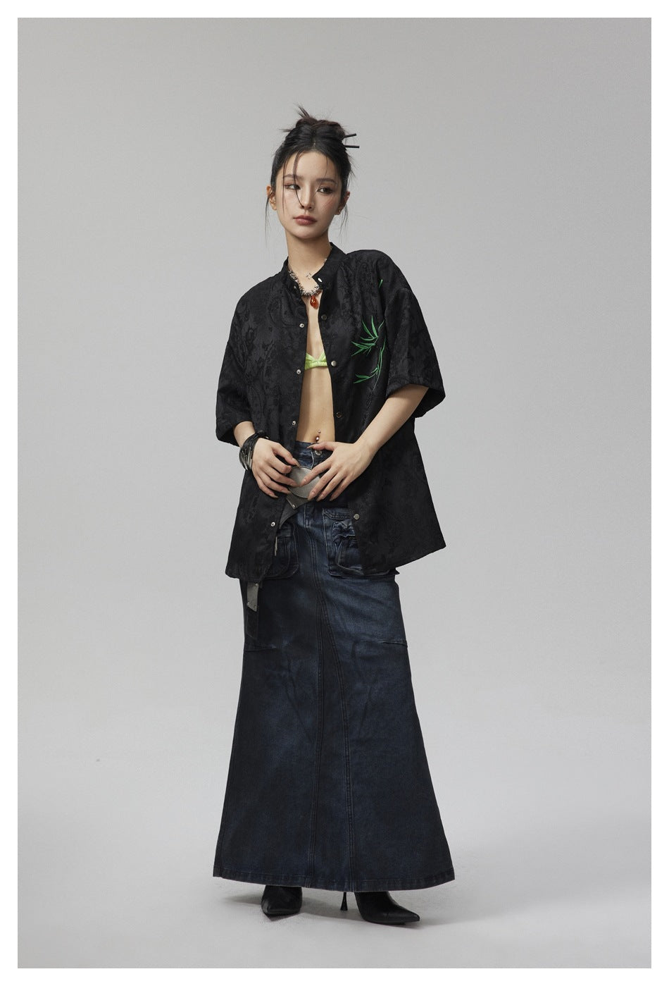 Full-length model wearing an oversized black patterned short-sleeve shirt with green branch embroidery.