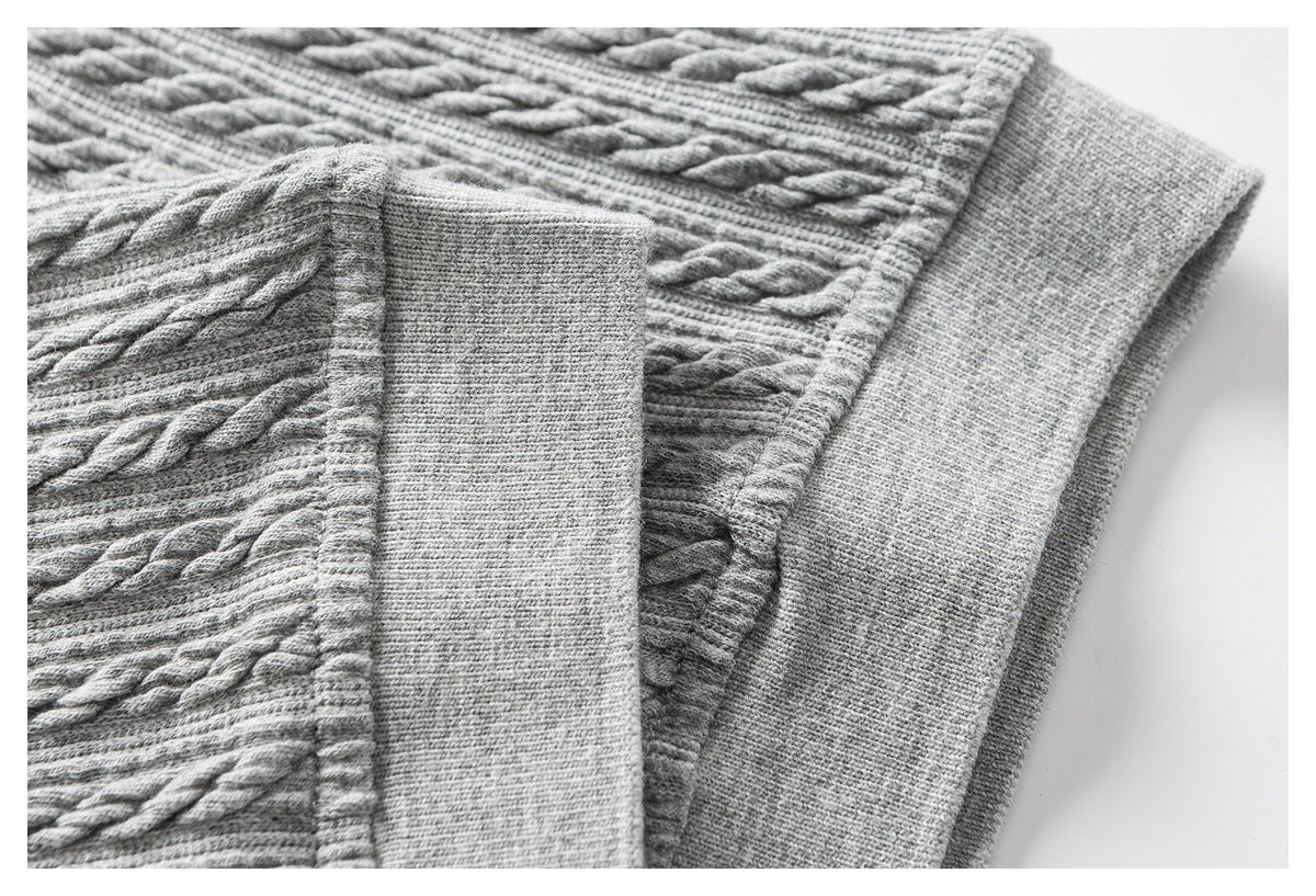 Close-up of light gray cable-knit fabric and a wide ribbed cuff beside a folded section.