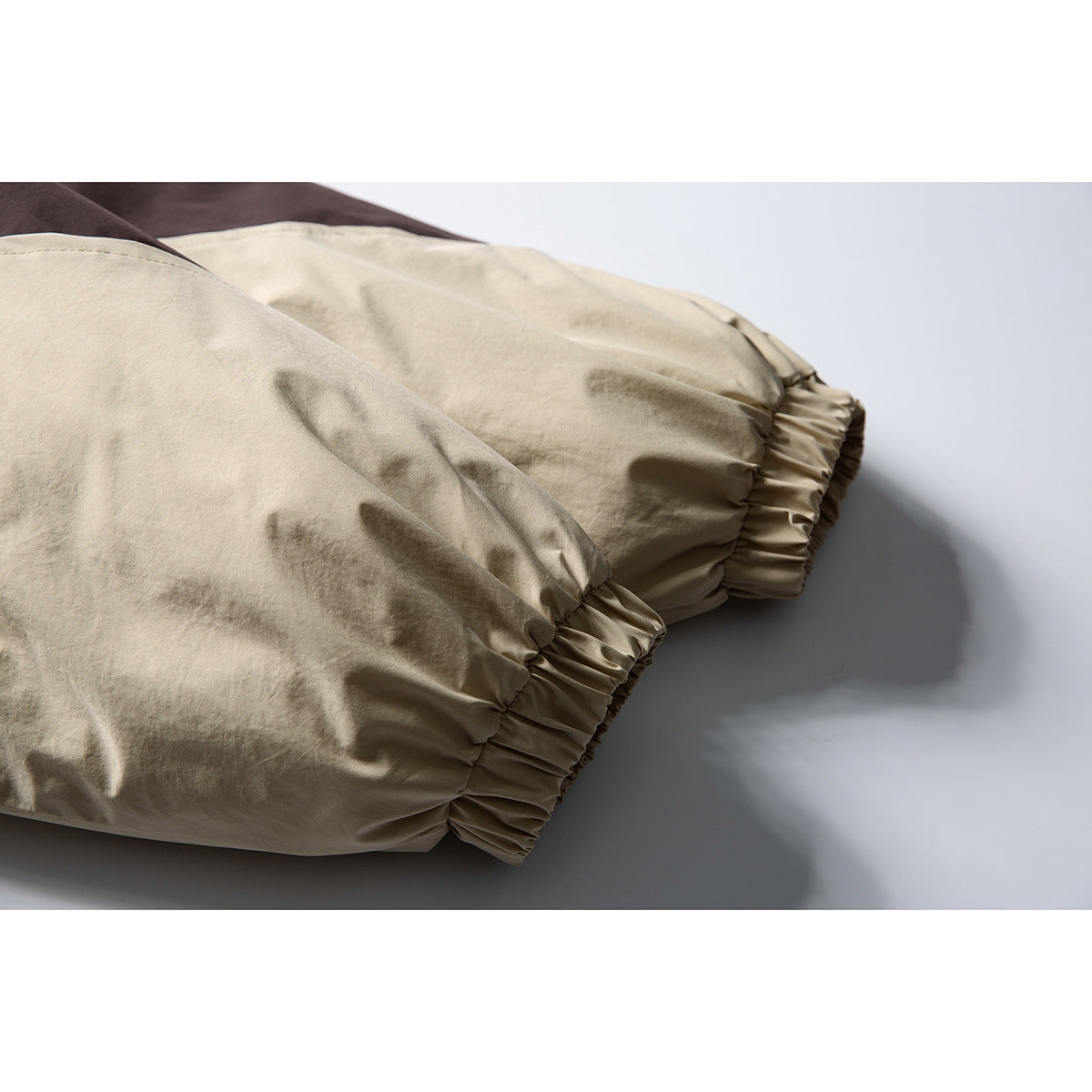 Close-up of a tan jacket sleeve with a gathered elastic cuff and dark brown fabric visible behind it.