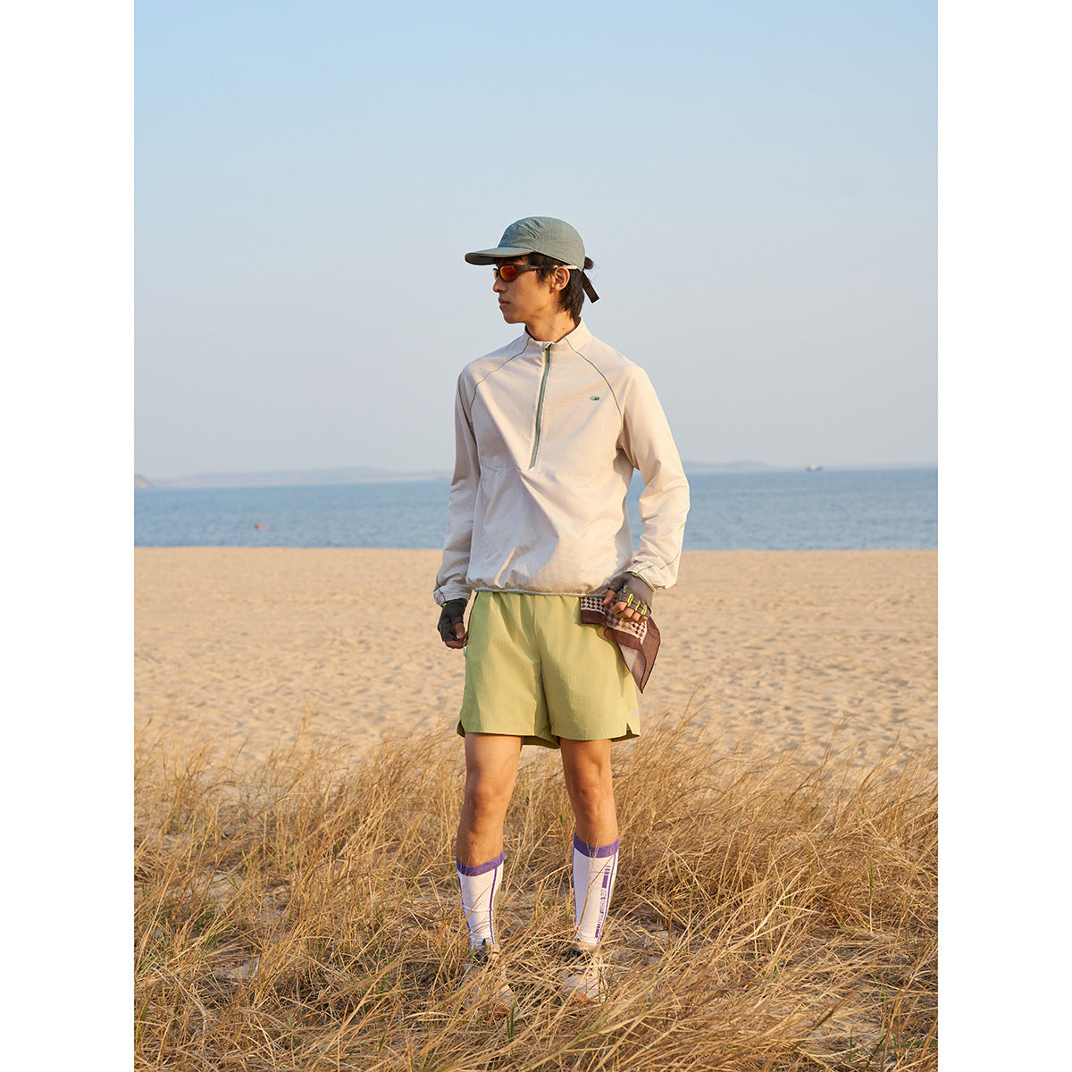 Person standing on a beach in a light pullover and pale yellow-green shorts with white socks.