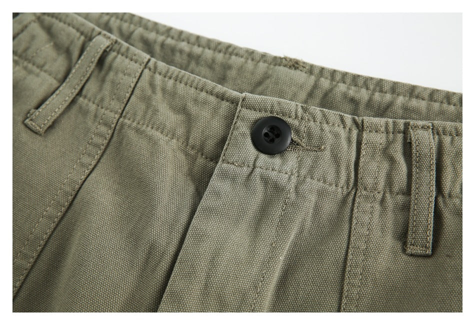 Close-up of olive trousers showing the waistband, black button, belt loops and pocket stitching.