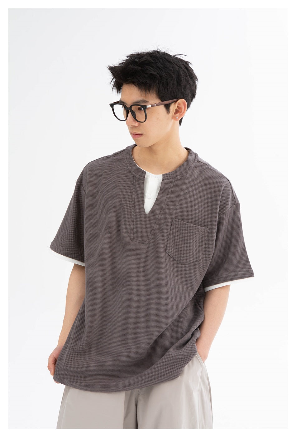 Close view of a model wearing a charcoal-gray textured short-sleeve shirt with white trim, split neckline, and chest pocket.