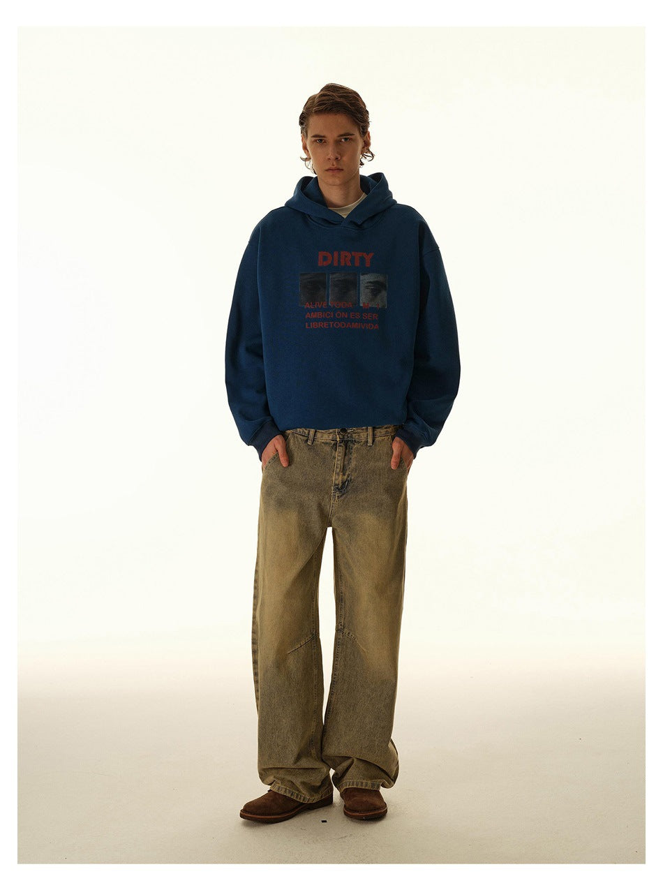 Model standing with hands in pockets wearing loose washed wide-leg jeans, blue graphic hoodie and brown shoes