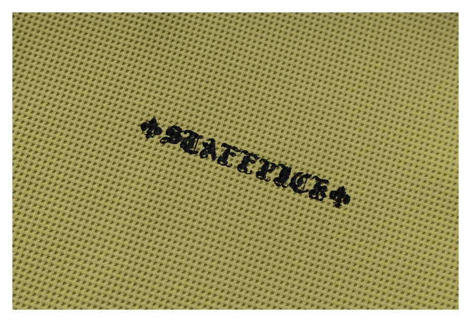 Close-up of black embroidered lettering on olive-yellow perforated knit fabric.