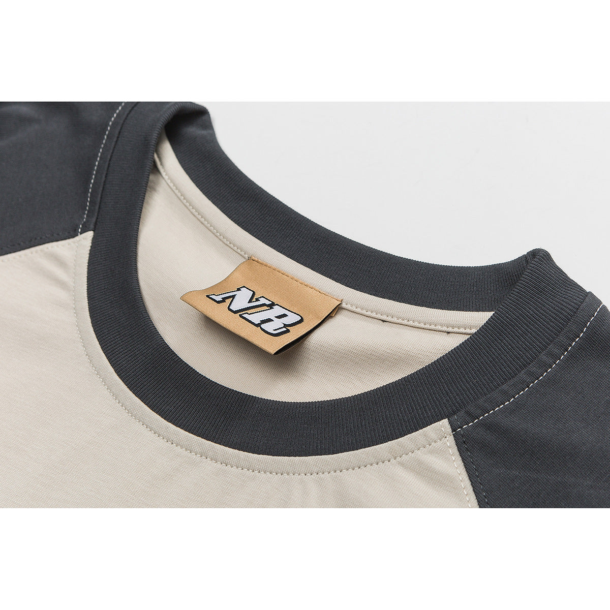 Close-up of a cream shirt with a dark ribbed neckline and a tan NB label.
