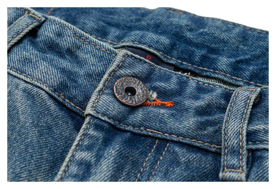 Close-up of blue denim jeans showing the waistband button, belt loop, and orange stitching.