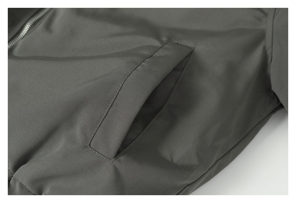 Close-up of a slanted welt pocket and zipper on a dark gray jacket.