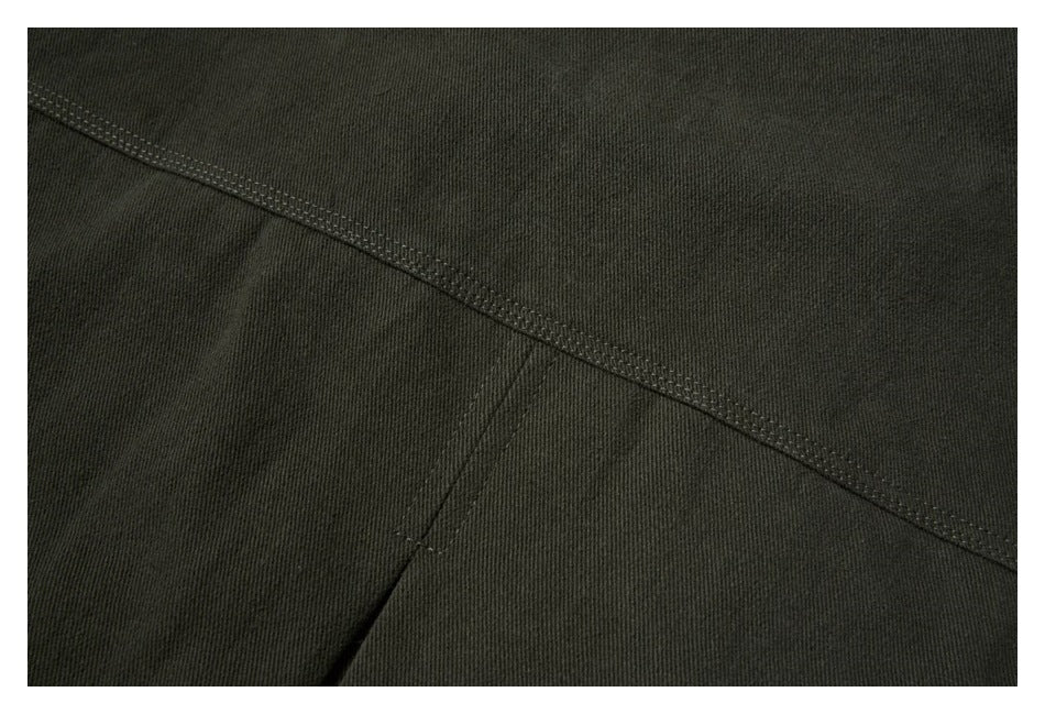Close-up of dark olive garment panels with a diagonal stitched seam and a vertical seam.