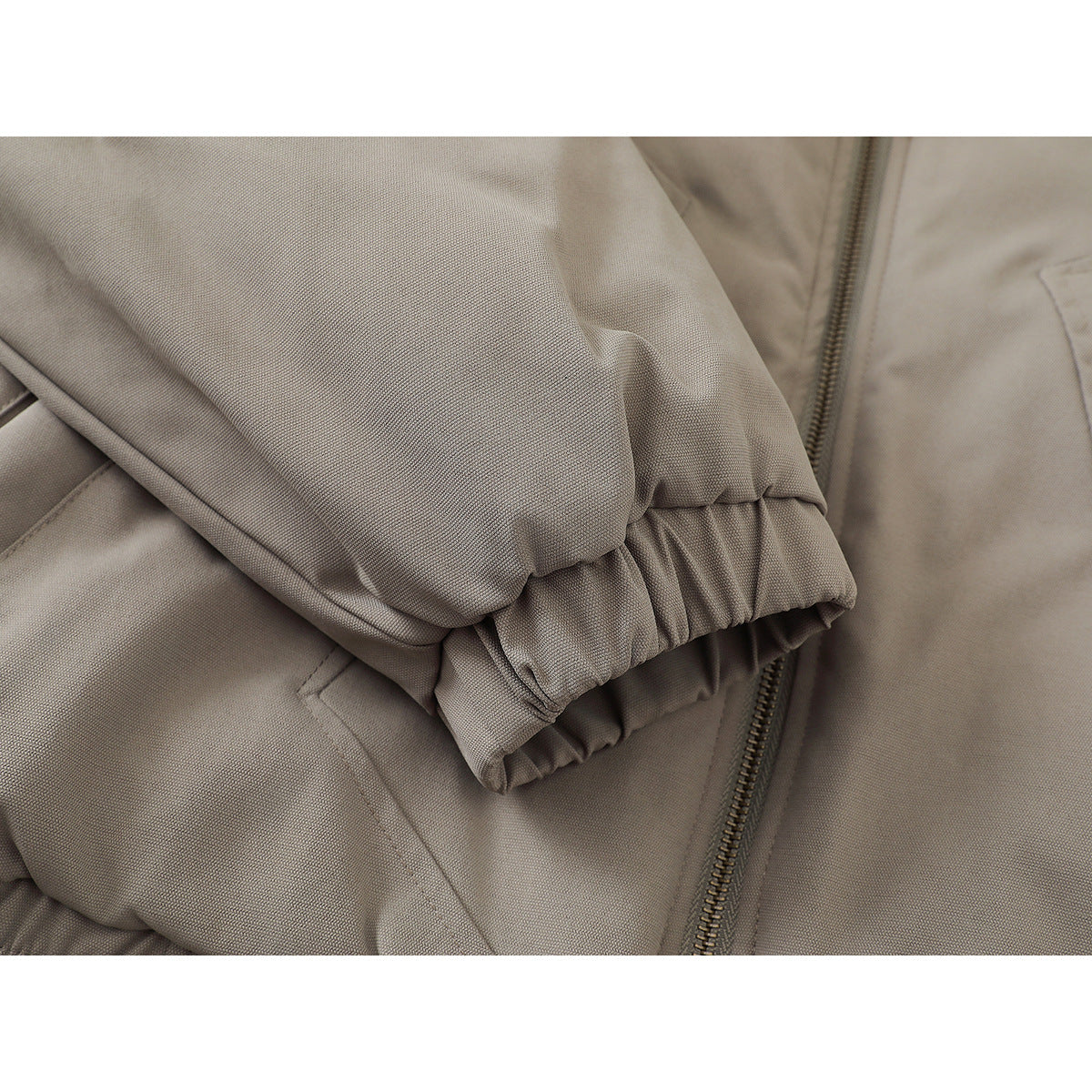 Close-up of a taupe jacket sleeve with an elastic cuff beside the front zipper.
