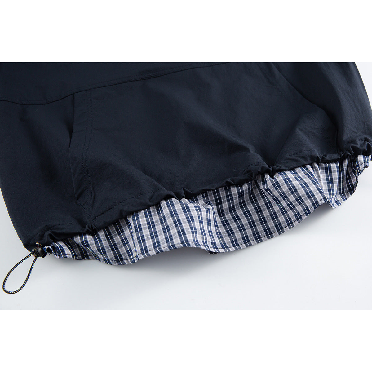 Close-up of a navy garment hem with a plaid lining and an adjustable drawcord.