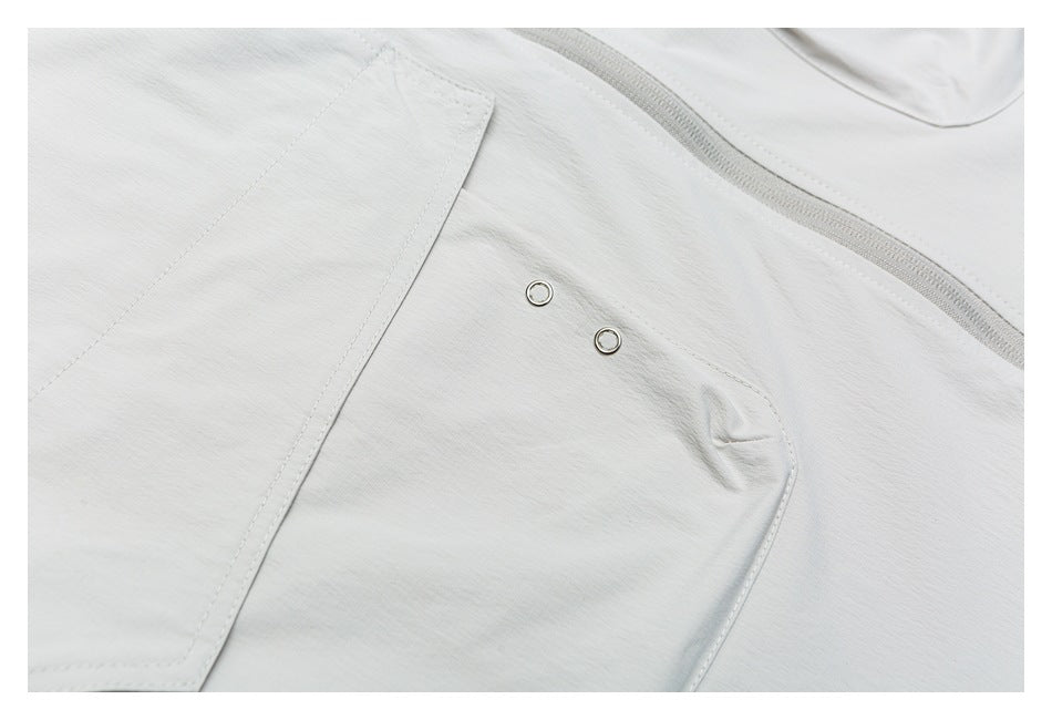 Close-up of a pale gray garment panel with two metal eyelets, a curved stitched section, and a zipper edge.