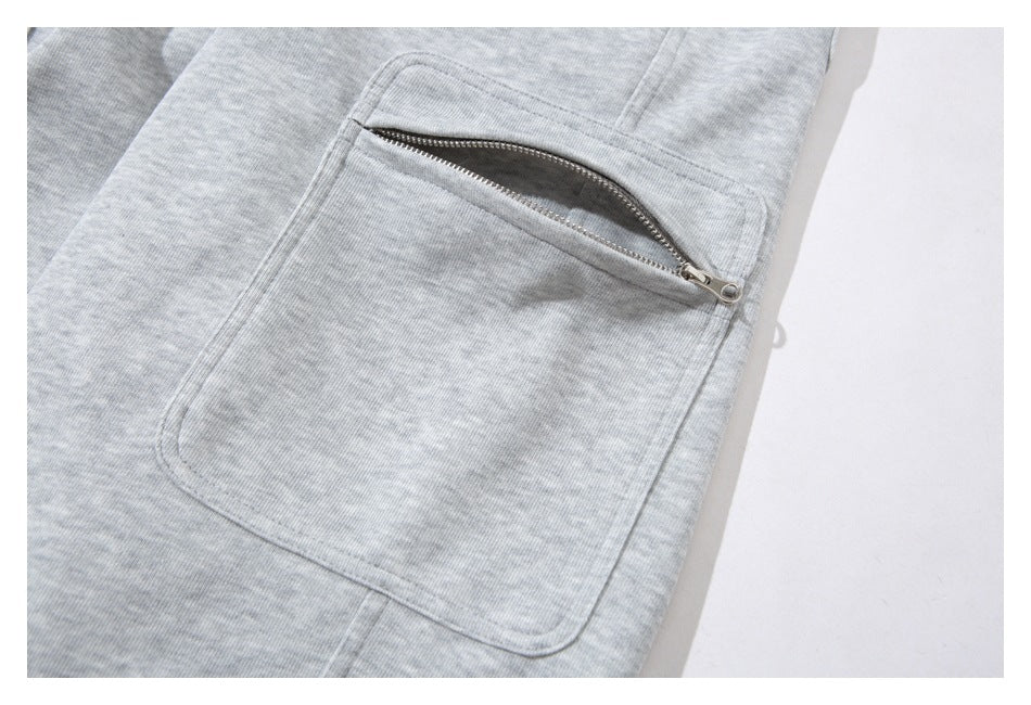 Close-up of light gray sweatpants showing a large pocket with a metal zipper.