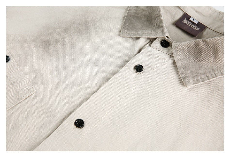 Angled close-up of beige shirt collars, black buttons, and a chest pocket edge.