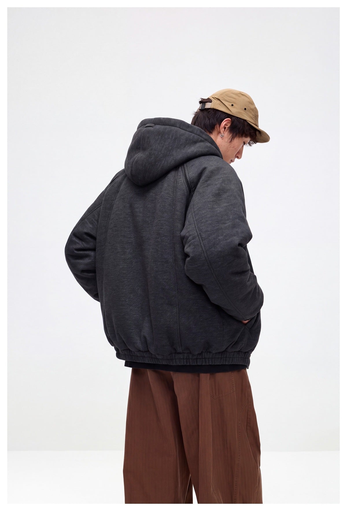 Rear three-quarter view of a model wearing a charcoal hooded jacket with a gathered hem.