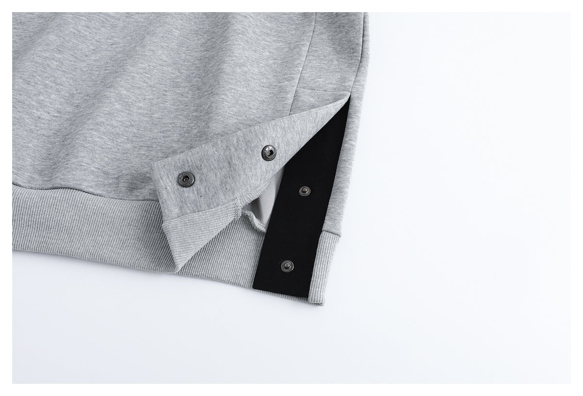Close-up of the light gray sweatshirt hem opened to show snap fasteners and a black inner panel.