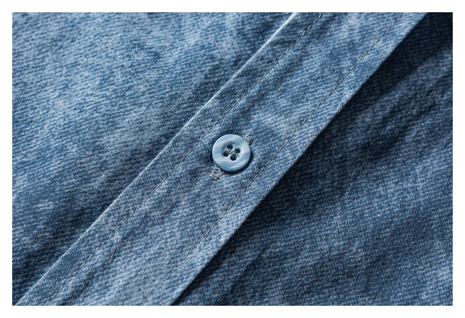 Close-up of a light blue button and stitched placket on mottled blue denim.