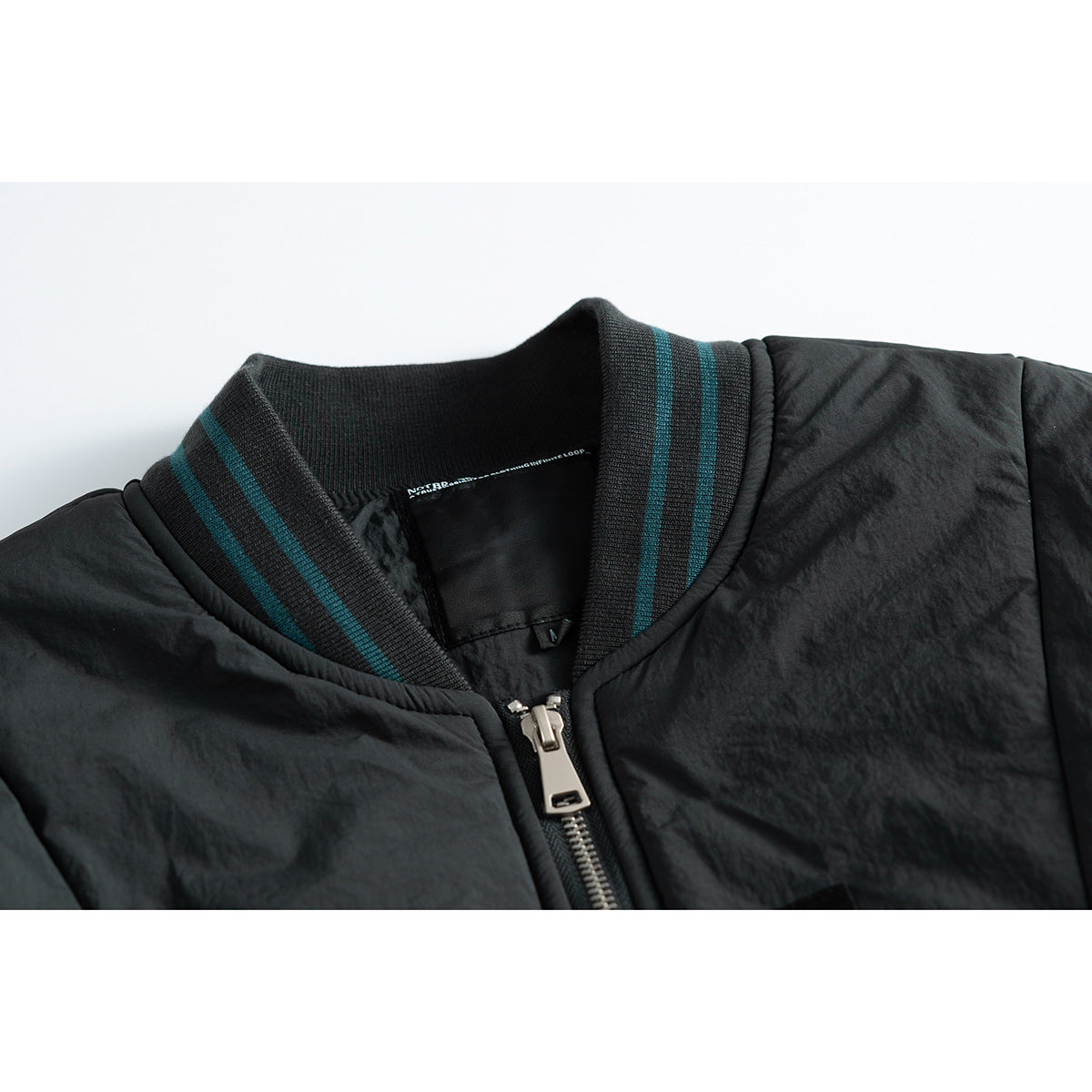 Close-up of a black jacket collar with teal stripes, a silver front zipper, and a small inner neck label.