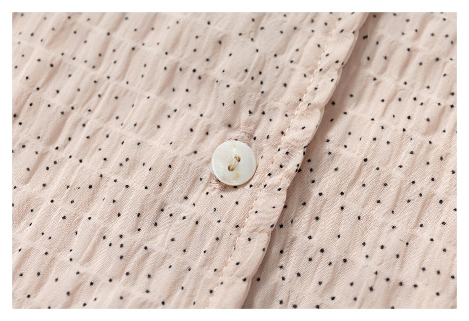 Close-up of a pearly button and stitched placket on pale blush fabric with tiny black dots.