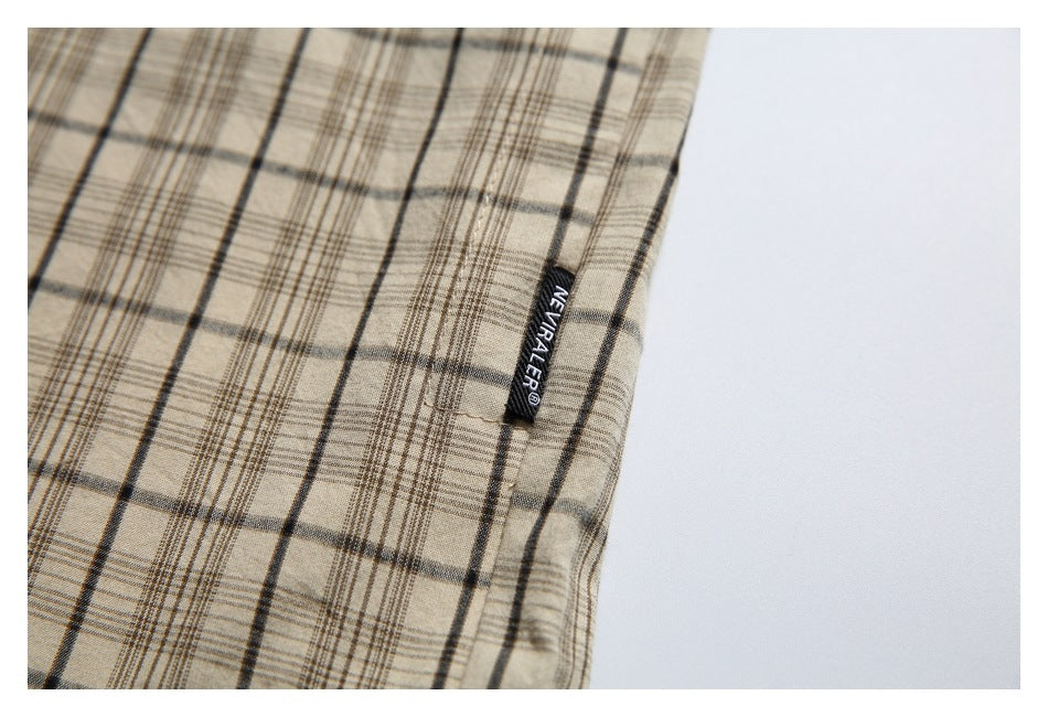 Close-up of a beige plaid shirt seam with a small black woven label bearing English lettering.