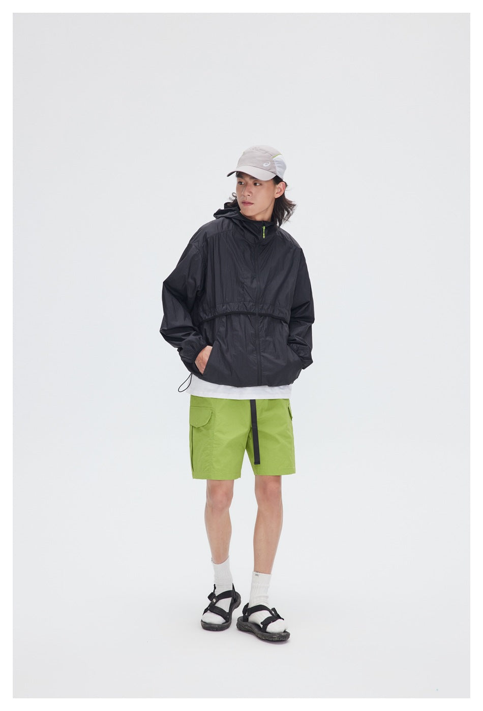 Model wearing a black hooded pullover jacket with lime-green shorts, white shirt, and light cap.