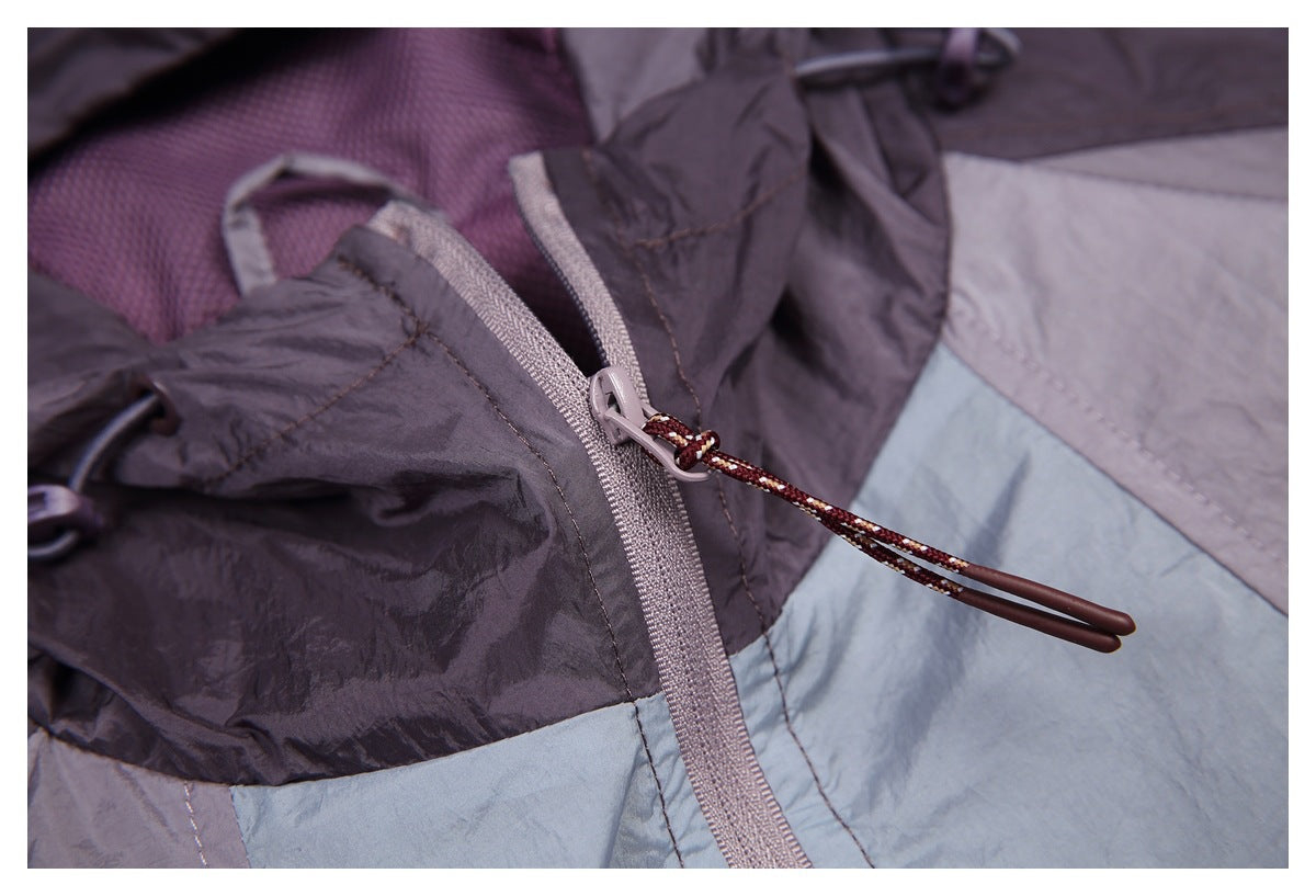 Close-up of a jacket zipper with a long corded pull against purple-gray and pale blue panels.