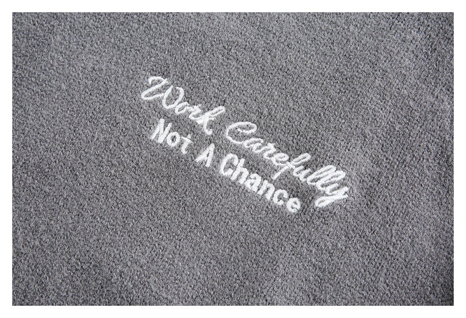 Close-up of gray knit fabric with white embroidery reading “Work Carefully Not A Chance.”