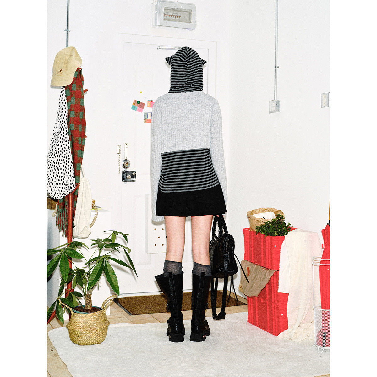 Back view of the model wearing a striped hooded top, cropped light-gray cardigan, and black skirt.