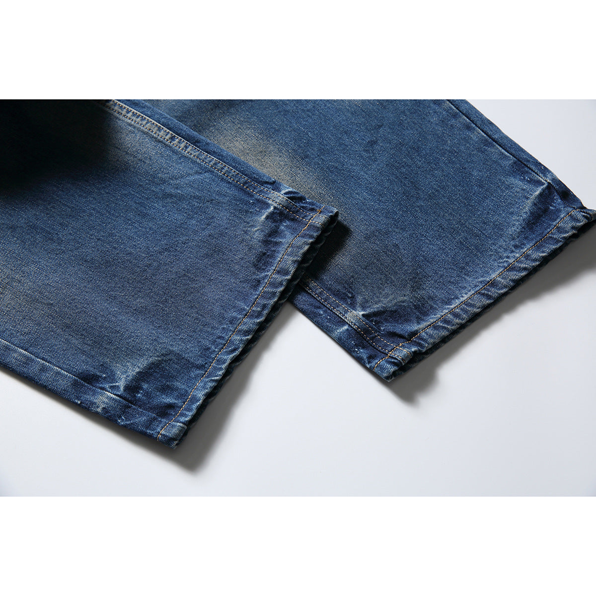 Close-up of the stitched hems and legs of blue faded jeans.