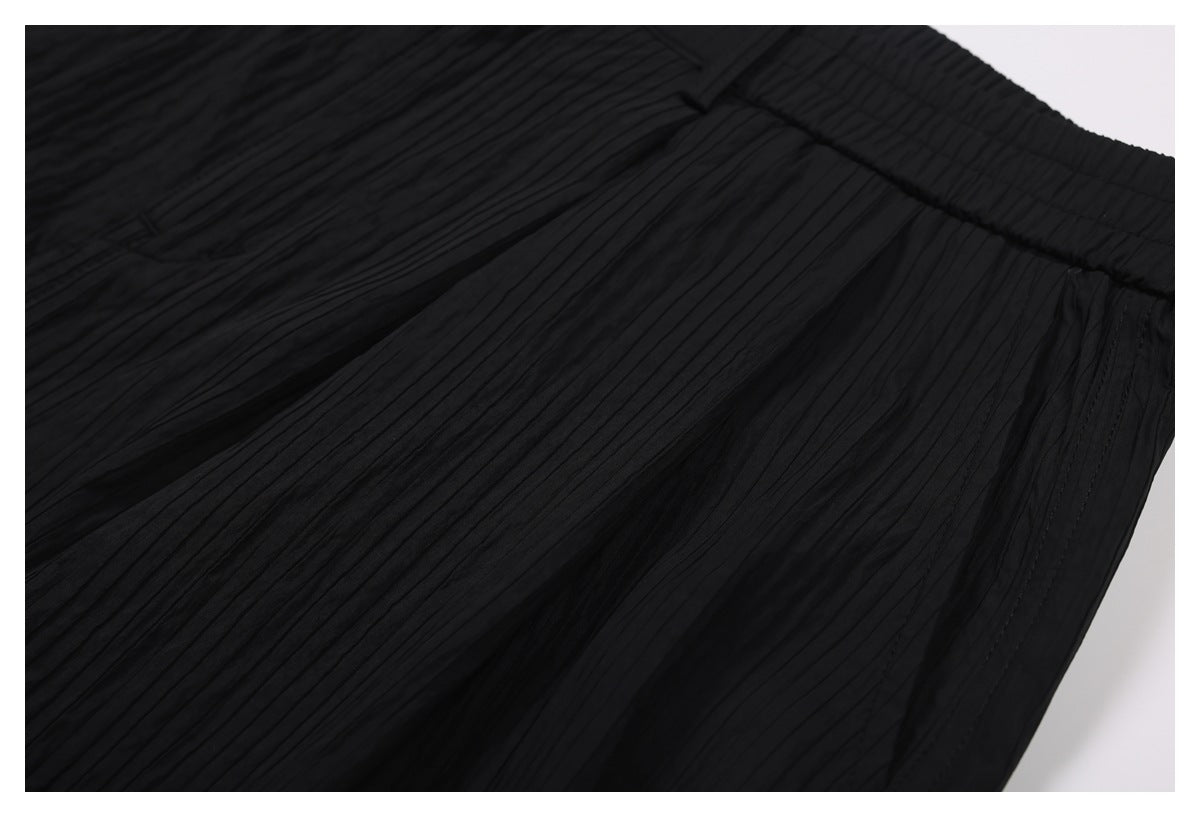 Close-up highlighting the narrow vertical pleats and waistband of black trousers.
