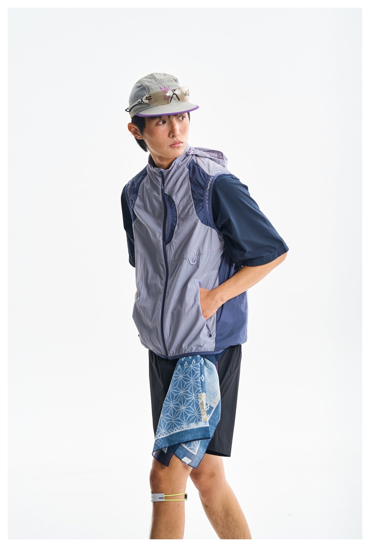 Model in a lavender and navy zip-front vest over a navy shirt, shown in a turned pose with black shorts.