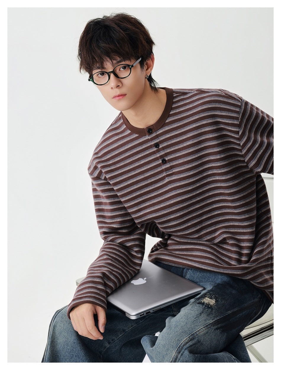 Seated model in a brown striped long-sleeve henley-style top with three buttons and loose jeans