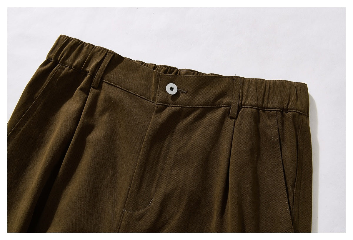Close-up of dark brown trousers showing an elasticated waistband, button, belt loops and front pleats.