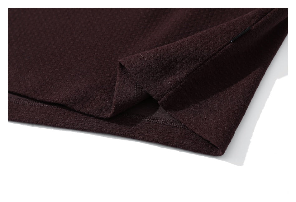 Close-up of a burgundy jacket's hem construction, showing a folded edge and visible stitching.