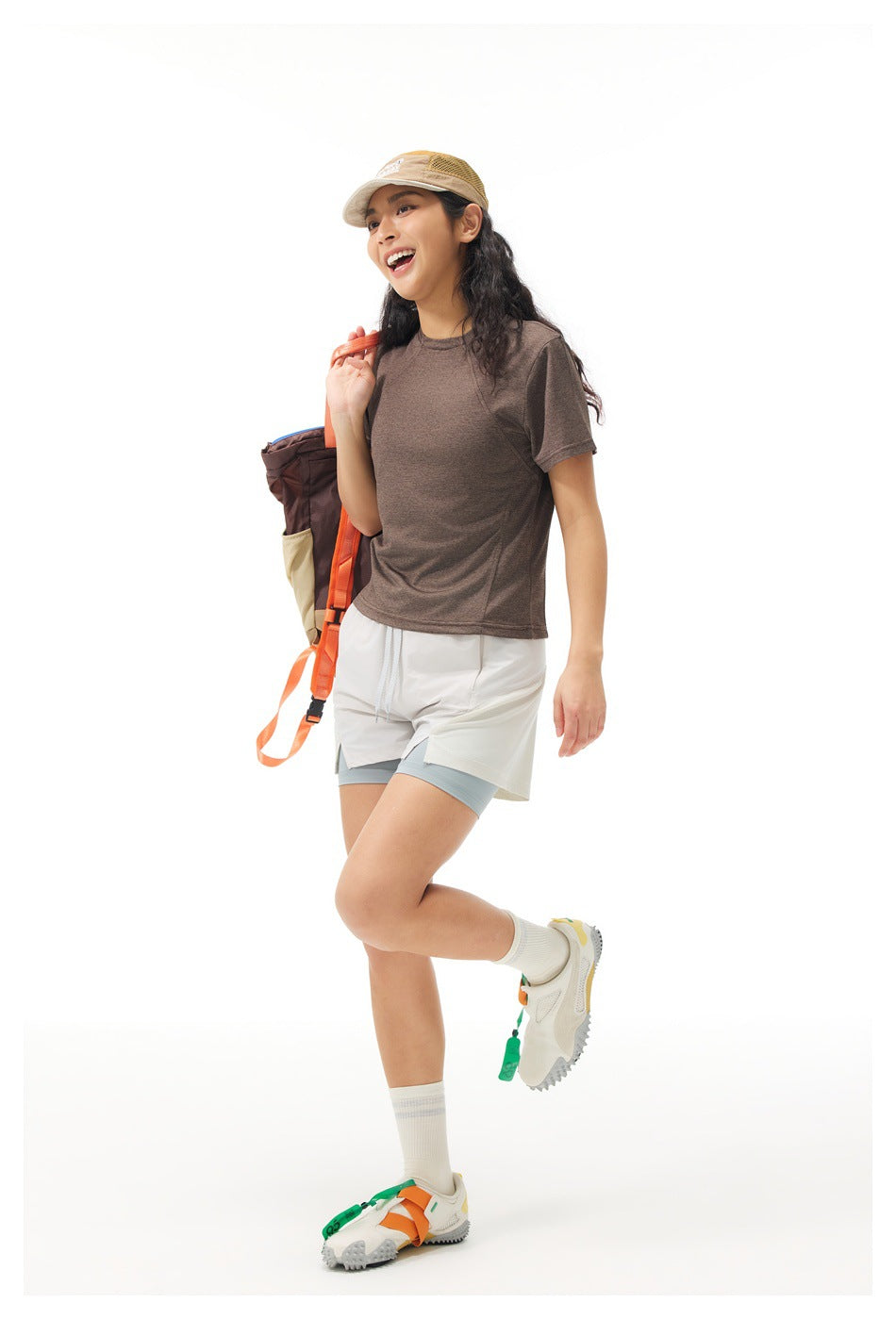 Model wearing a brown short-sleeve athletic shirt and layered white shorts, shown from the front.
