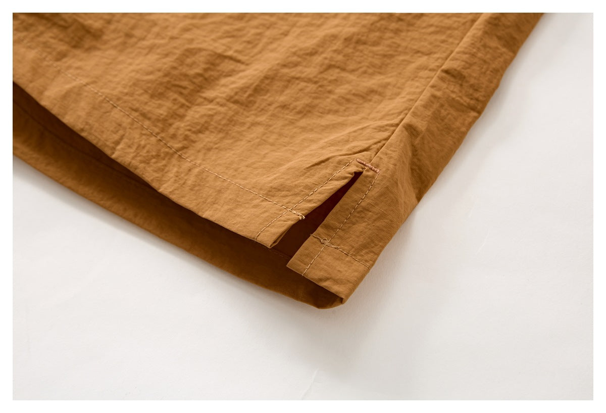 Close-up of the rust-brown shorts' hem, showing a short side slit and stitched edging.