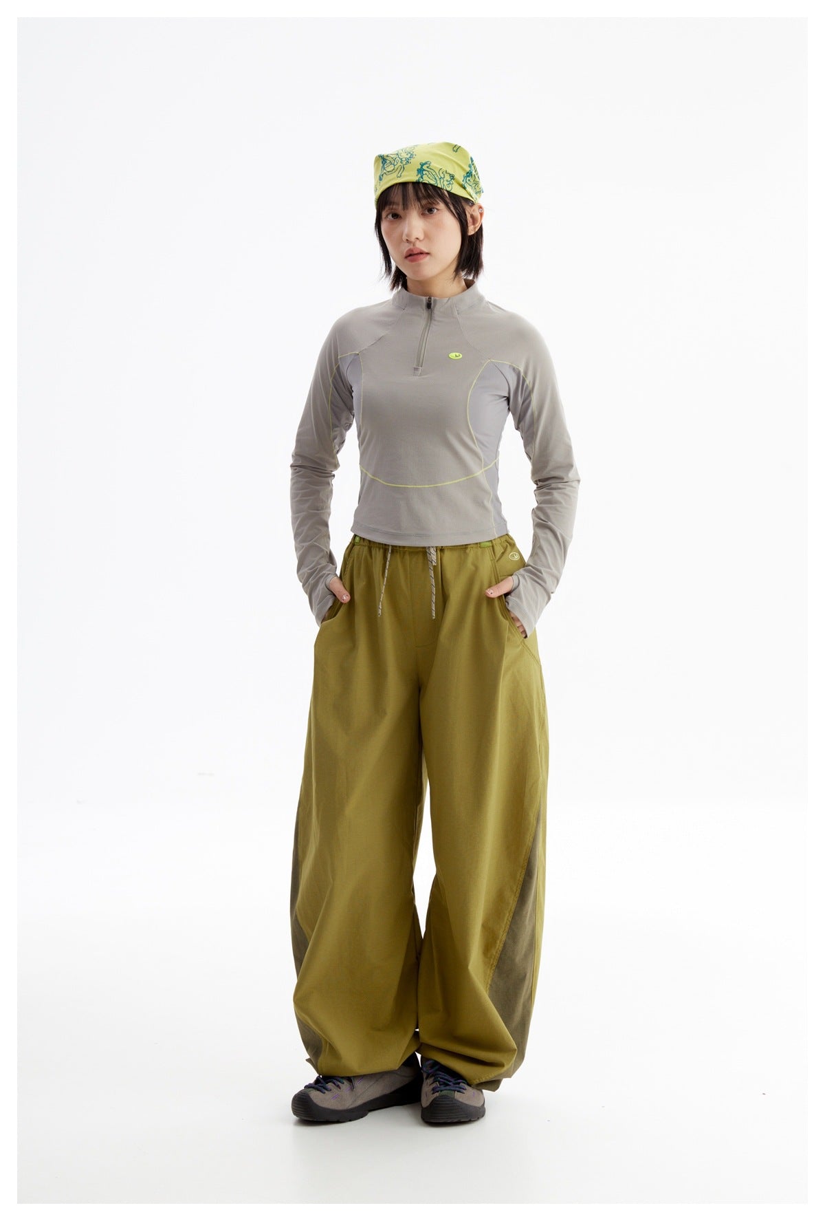 Model wearing a light gray quarter-zip top with lime accents and loose olive trousers, with a yellow patterned headscarf.