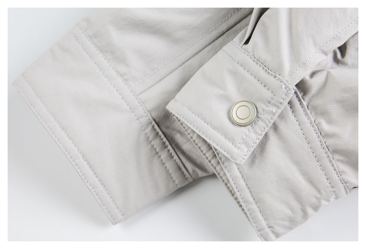 Pale gray garment cuff detail with a snap-fastened tab, stitched seams, and an adjacent fabric panel.