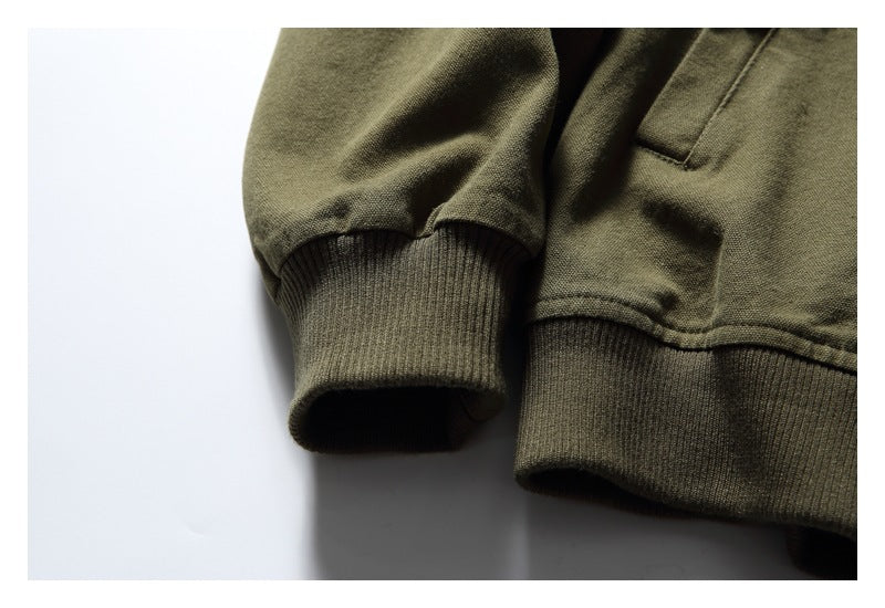 Close-up of an olive garment's ribbed sleeve cuff and lower band, with a pocket edge visible.
