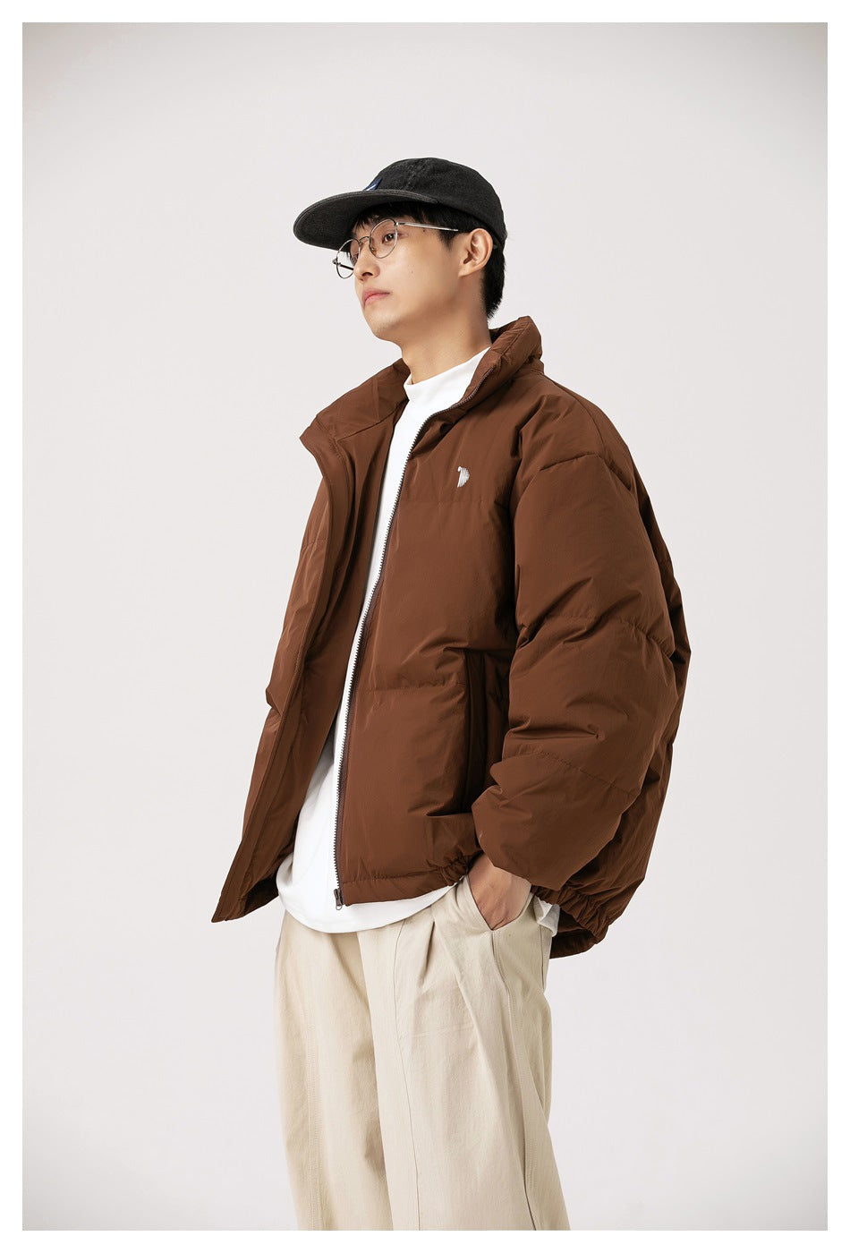 Angled front view of a person wearing a brown padded jacket with a high collar and small white chest emblem.