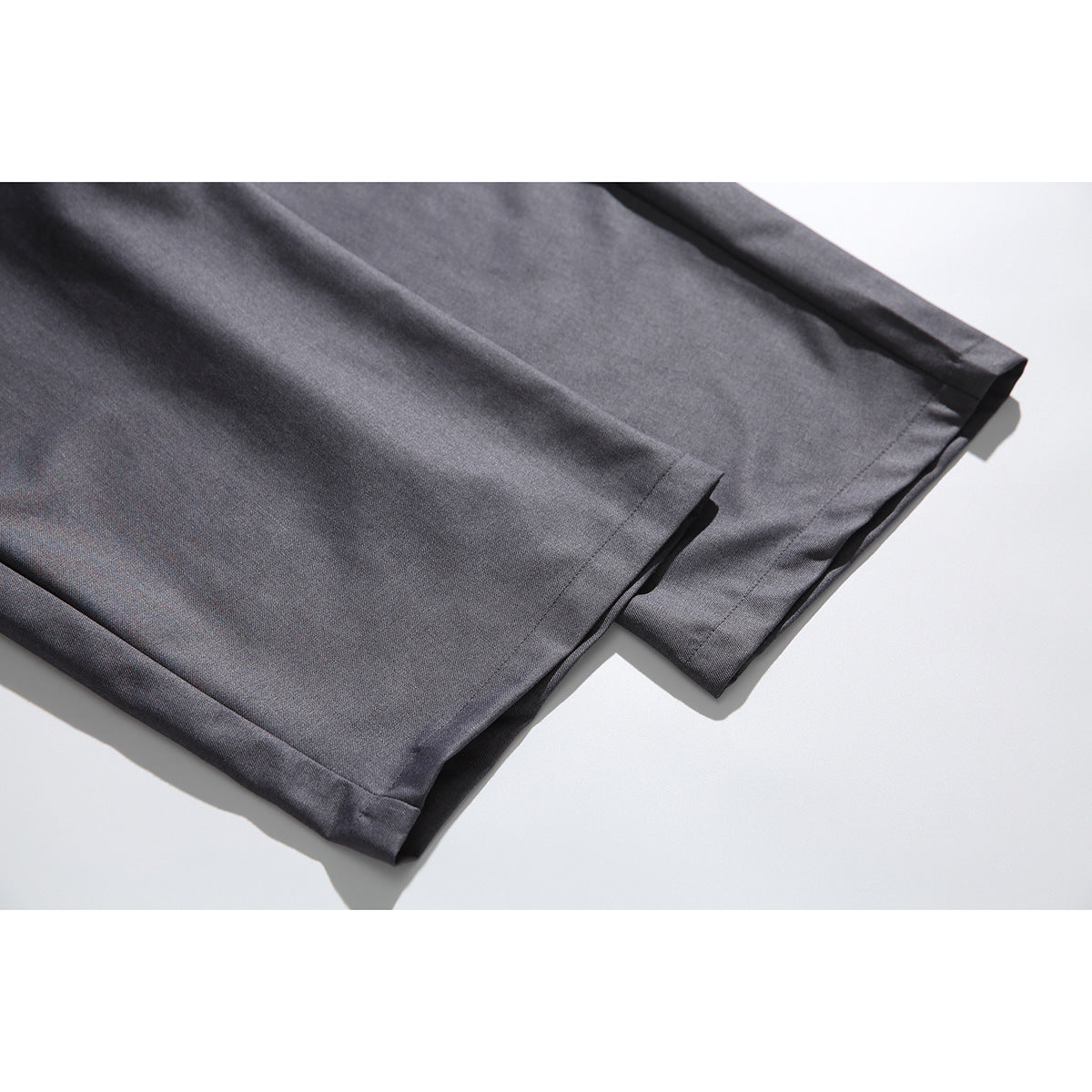 Close-up of the straight hems of charcoal-gray trousers laid flat.