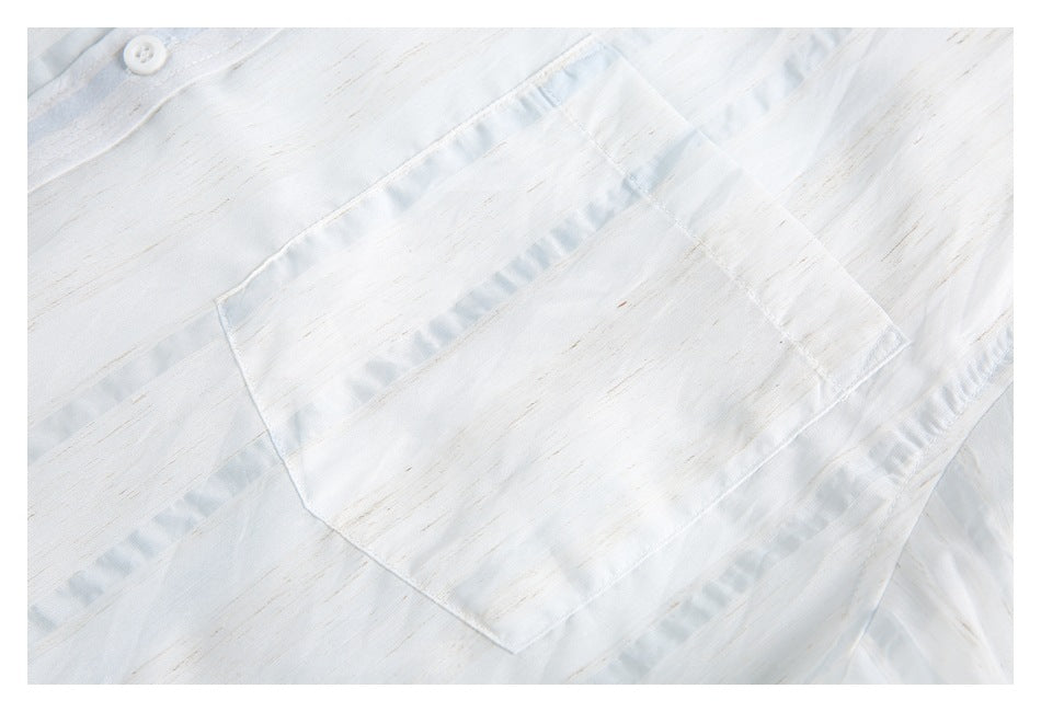 Close-up of a white shirt's stitched chest pocket and button, with subtle tan streaks and pale blue accents.
