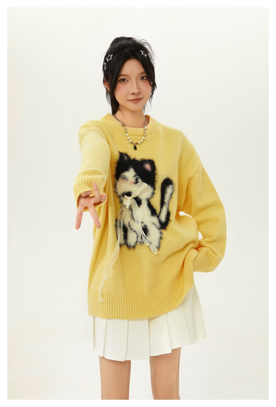Closer view of a model wearing a yellow sweater with a fuzzy cat graphic and a white pleated skirt.