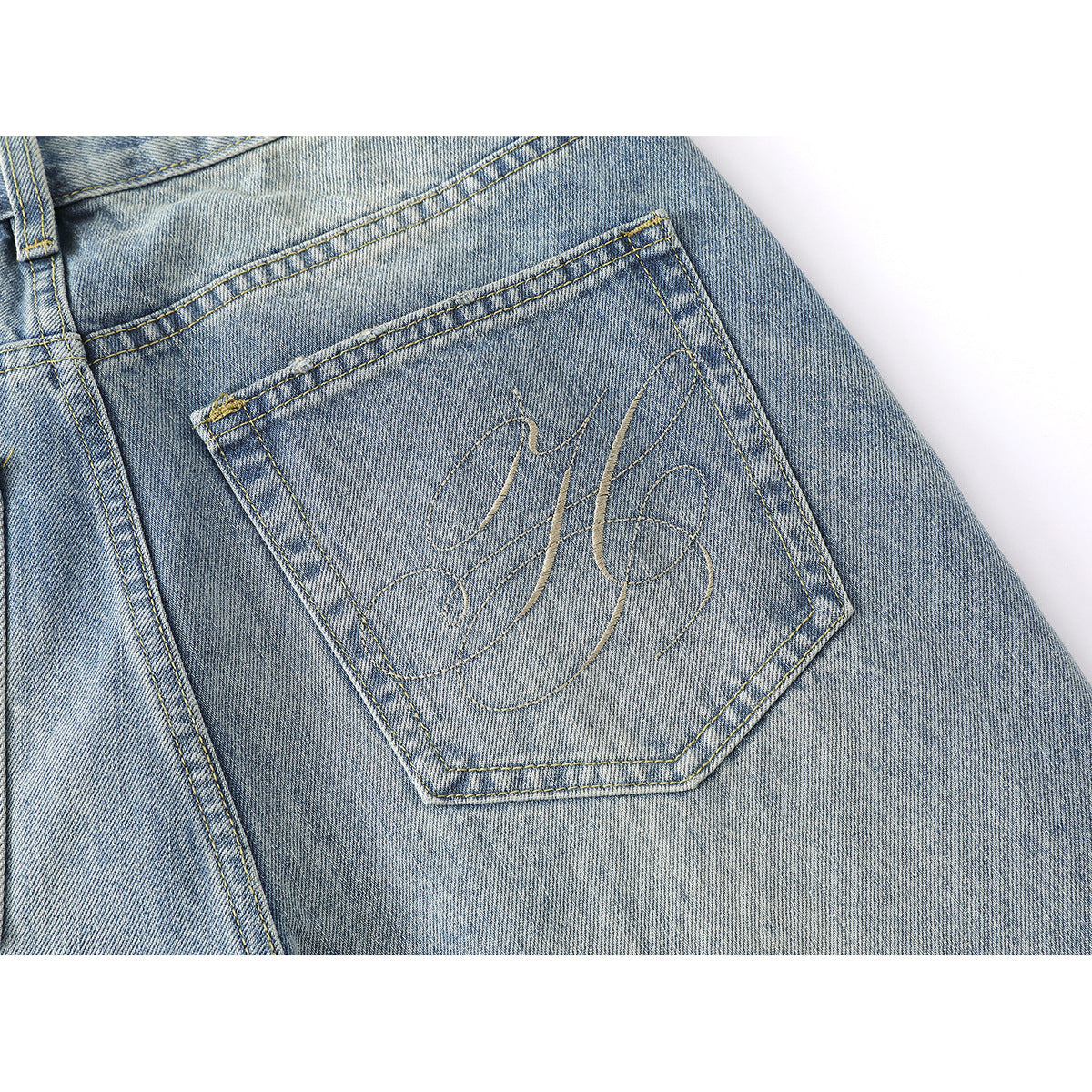 Close-up of a back pocket with decorative stitched lettering on light-wash blue jeans.
