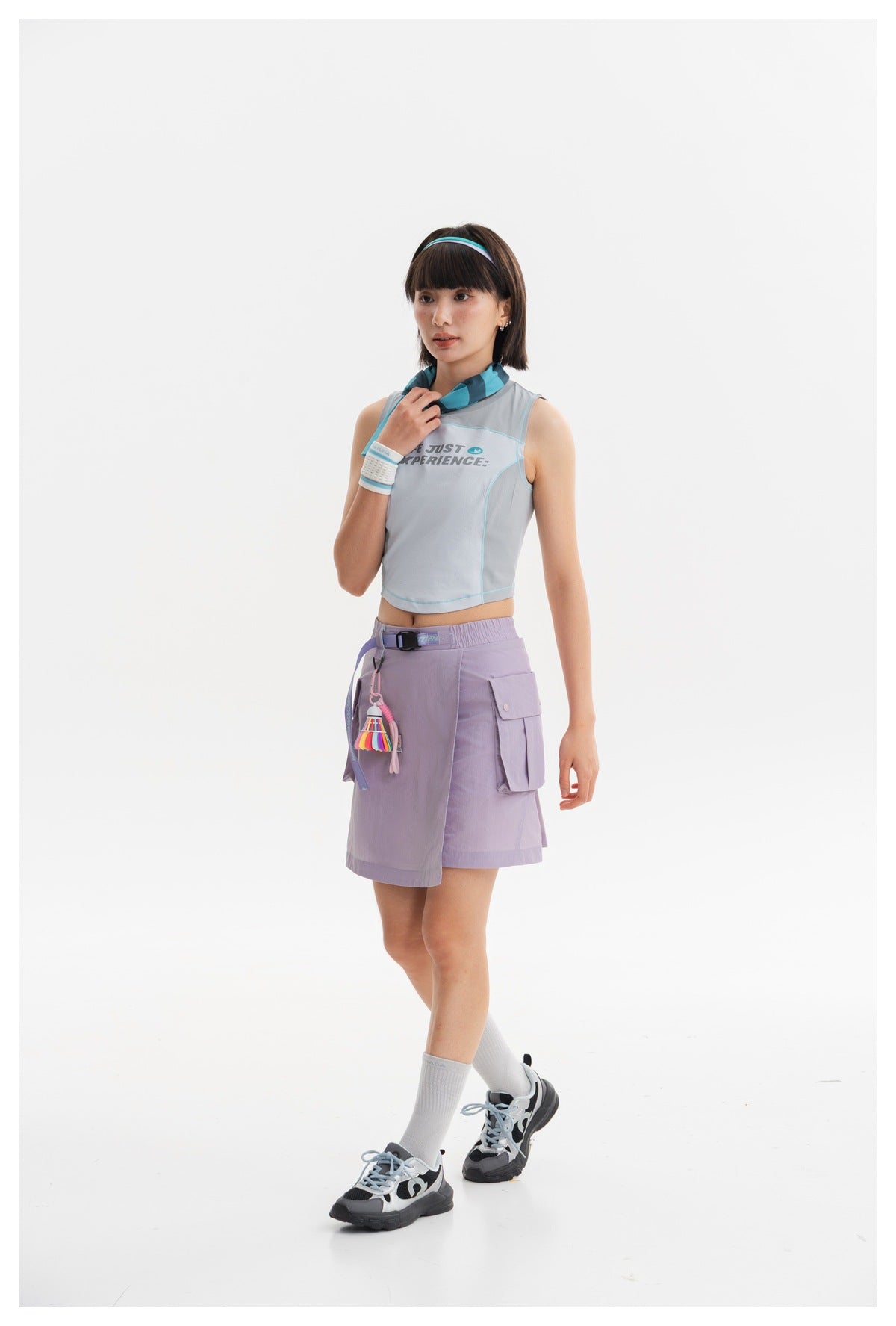 Model wearing a pale blue sleeveless crop top and lavender wrap-front cargo skirt, shown at a three-quarter angle.