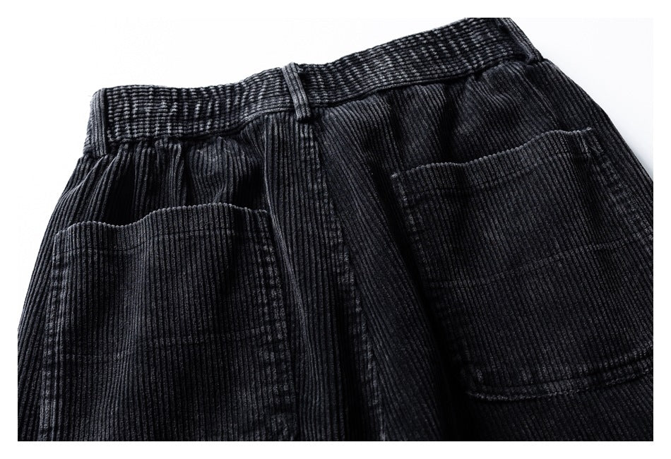 Close-up of the back waist and two patch pockets on black corduroy trousers.