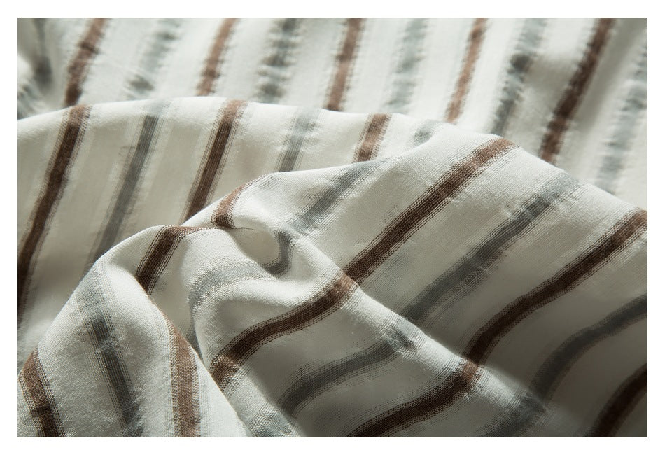 Draped close-up of off-white garment fabric with muted gray and brown stripes, showing its weave and folds.