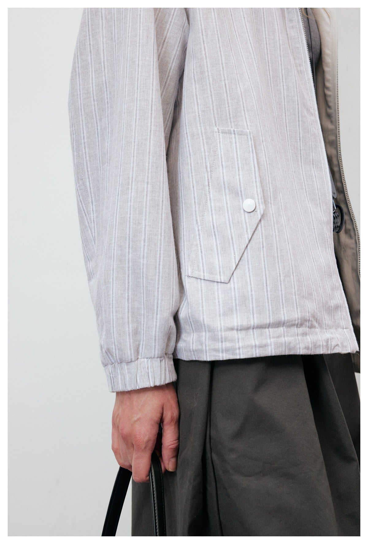 Close-up of the pale gray striped jacket's angled flap pocket, white snap, and gathered cuff.