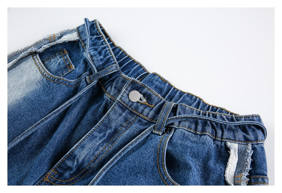 Close-up of blue denim jeans showing the front waistband, button, belt loops, and front pocket.