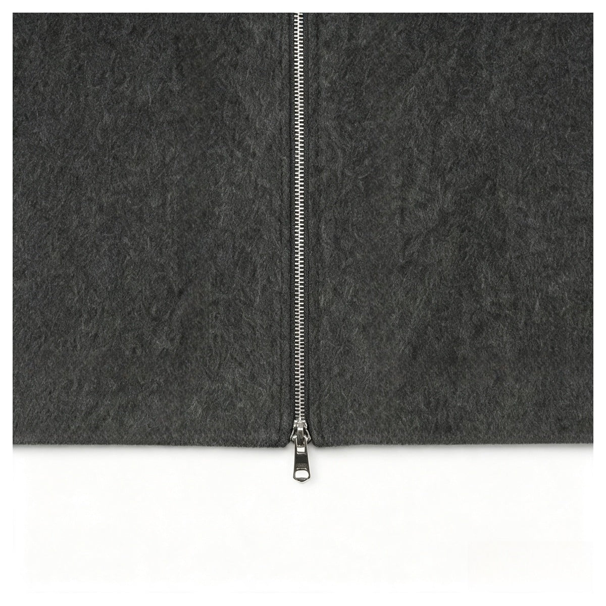 Close-up of the lower end of a silver zipper on charcoal gray fabric.